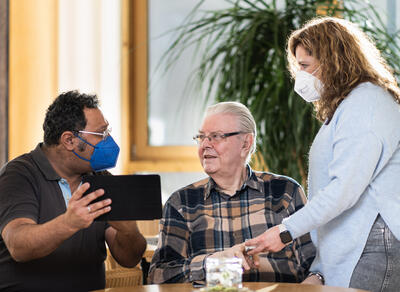 Bild vergr��ern: DataHealth-Studienarzt Prof. Dr. med. Nabeel Farhan (links) kann auf seinem mobilen Ger�t direkt die von Bernhard Klein (Mitte) gemessenen Vitaldaten einsehen. Der Bewohner des Christlichen Seniorenhauses in L�tzeln wird dabei von der Pflegedienstleiterin Daniela D�rr (rechts) unterst�tzt. Eine Live-Demonstration gibt es beim Holzh�user �rztegespr�ch.