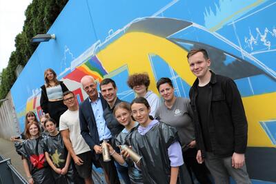 Bild vergr��ern: Graffiti-K�nstler Julian Irlich (6. v. l.) hat mit Sch�lerinnen und Sch�lern der Gemeinschaftlichen Sekundarschule die Mauer hinter dem Burbacher Bahnsteig neugestaltet.