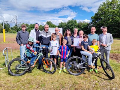 Bild vergr��ern: B�rgermeister Jonas Becker (r.) freut sich mit dem Vorsitzenden des F�rdervereins Matthias Moos (5.v.r.) sowie mit weiteren Mitgliedern des Vorstandes und einigen jugendlichen Stammg�sten des Mehrgenerationen-Sportplatzes �ber die Nominierung f�r den NRW-Engagementpreis 2026.